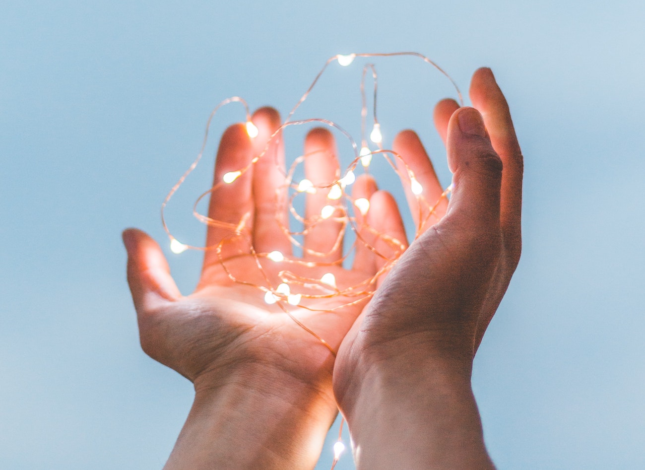 two hands holding string lights against a baby blue backdrop