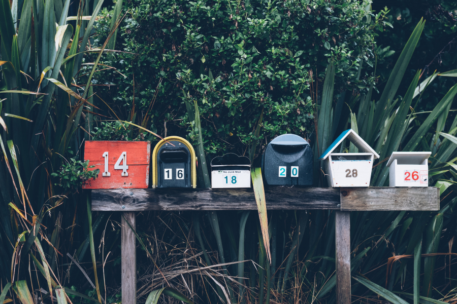 6 mail boxes with foliage in the back